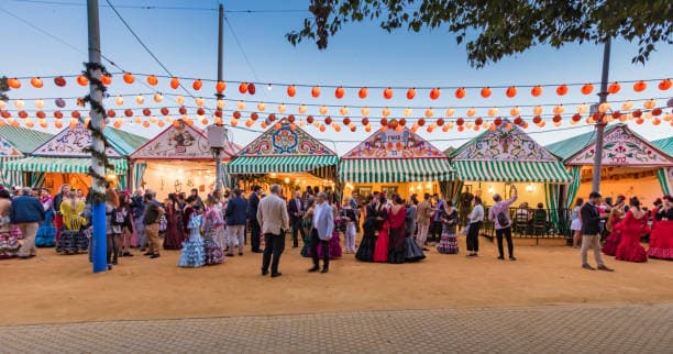 Feria de Abril de Sevilla: casetas iluminadas, ambiente nocturno y público con trajes de flamenca